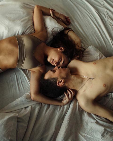 Two people lying close on white sheets in soft morning light